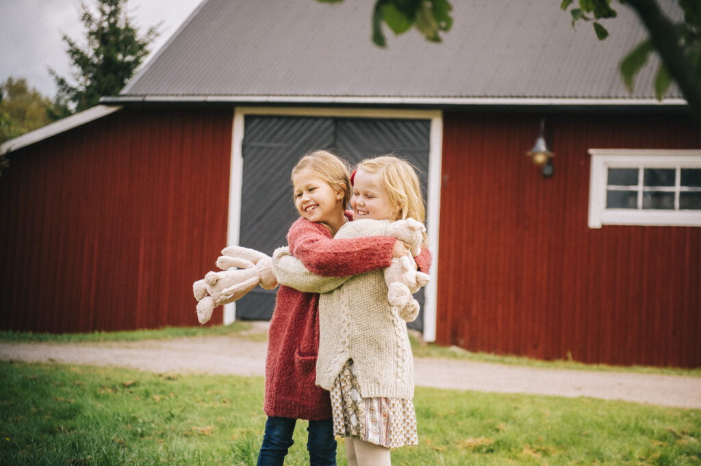 Lapset halaavat ulkona, taustalla punainen puurakennus.